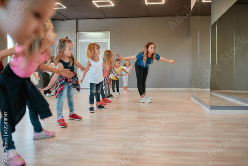 Fototapeta Naklejka Na Ścianę i Meble -  Warming up. Happy boys and girls doing stretching exercises with female dance teacher in the dance studio. Choreography concept