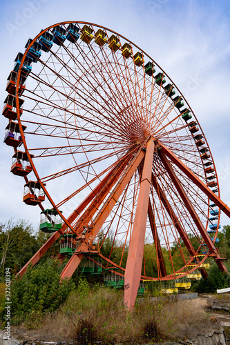 old abandoned red ferris wheel with colorful gondolas in sunny weather and blue sky
