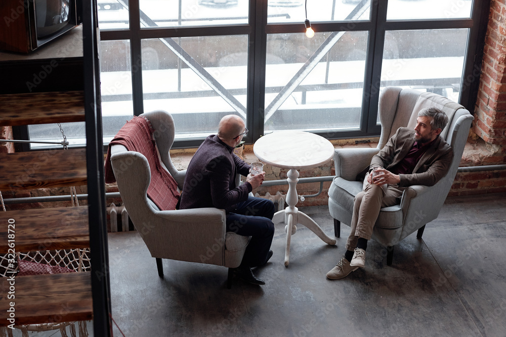 Above view of stylish middle-aged businessmen sitting in comfortable armchairs and drinking alcohol in lobby bar Above view of stylish middle-aged businessmen sitting in comfortable armchairs and drinking alcohol in lobby bar