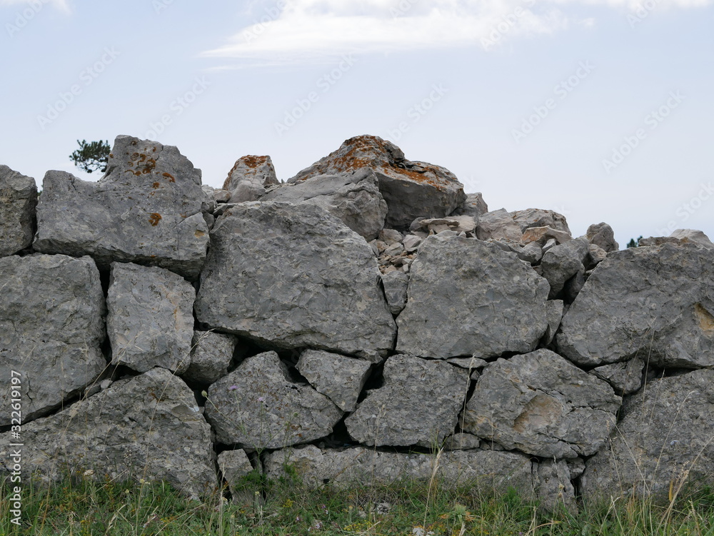 An ancient fence made of huge stones in the mountains of Crimea against the blue sky with white Cumulus clouds on a Sunny summer day. An ancient fence made of huge stones in the mountains of Crimea against the blue sky with white Cumulus clouds on a Sunny summer day.