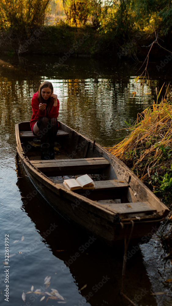 curly girl sitting on the edge of an abandoned wooden boat at sunset.