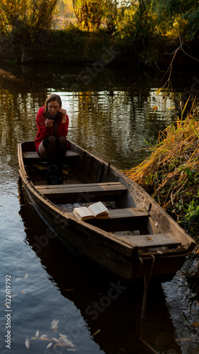 curly girl sitting on the edge of an abandoned wooden boat at sunset.