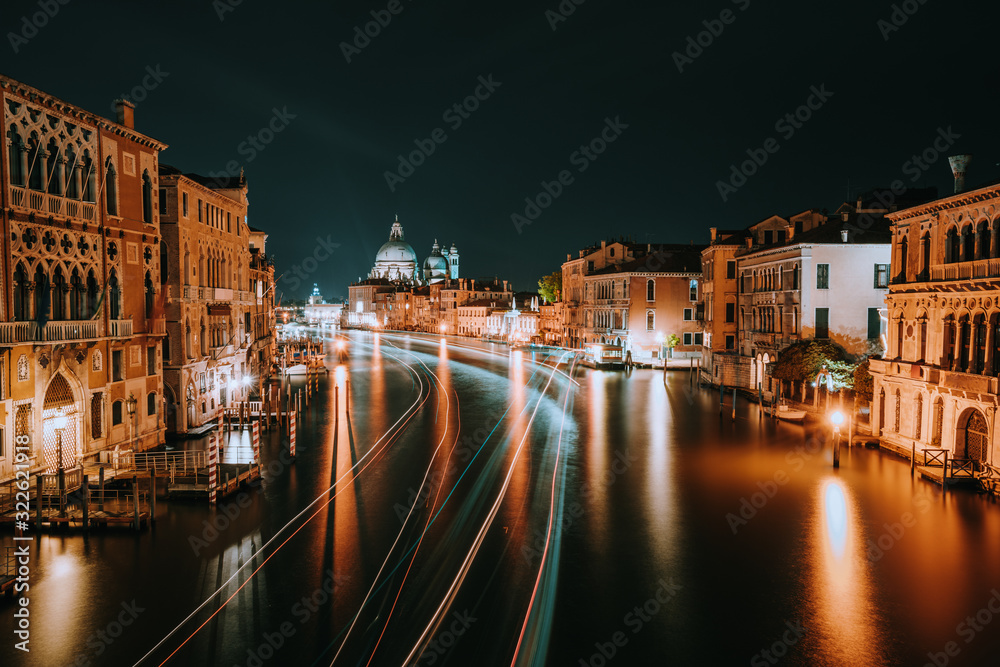 Venice night scenery. Light illuminated trails of ferries and boats reflected on the Grand Canal surface. Majestic Basilica di Santa Maria della Salute in background. Italy