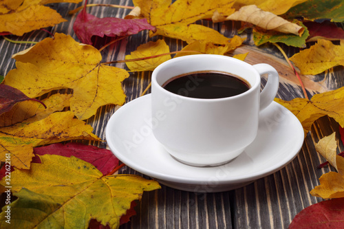 White cup of coffee on wooden table and autumn yellow leaves around.