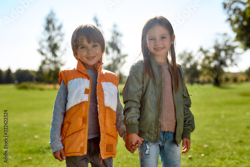 Happy together. Portrait of cute brother and sister holding hands and looking at camera with smile while standing in the park