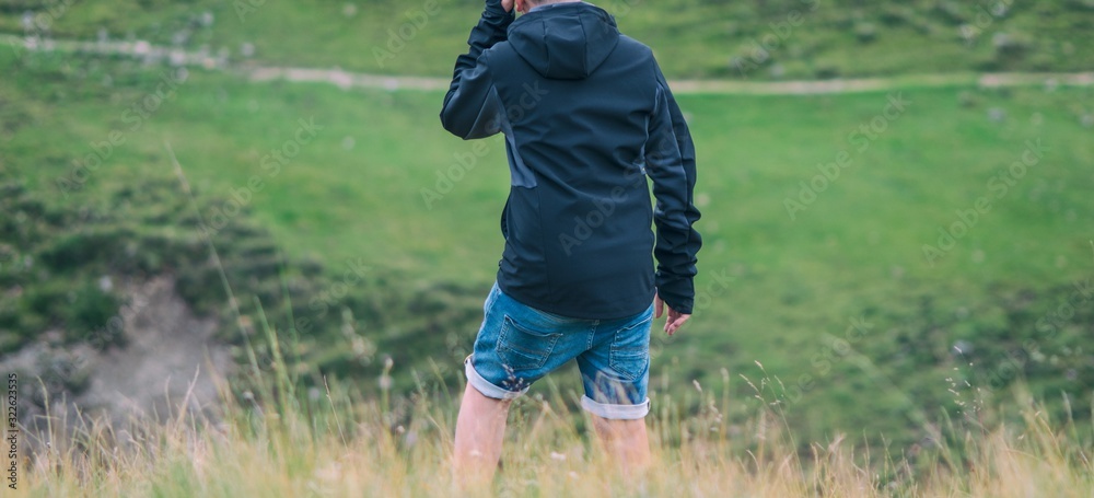 A young guy standing in a field full of grass looking at the mountains. A young guy standing in a field full of grass looking at the mountains.