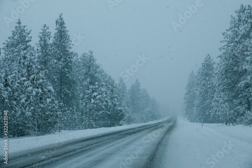 Empty road in Idaho crosses the snowy spruce forest during an intense snowstorm. © helivideo