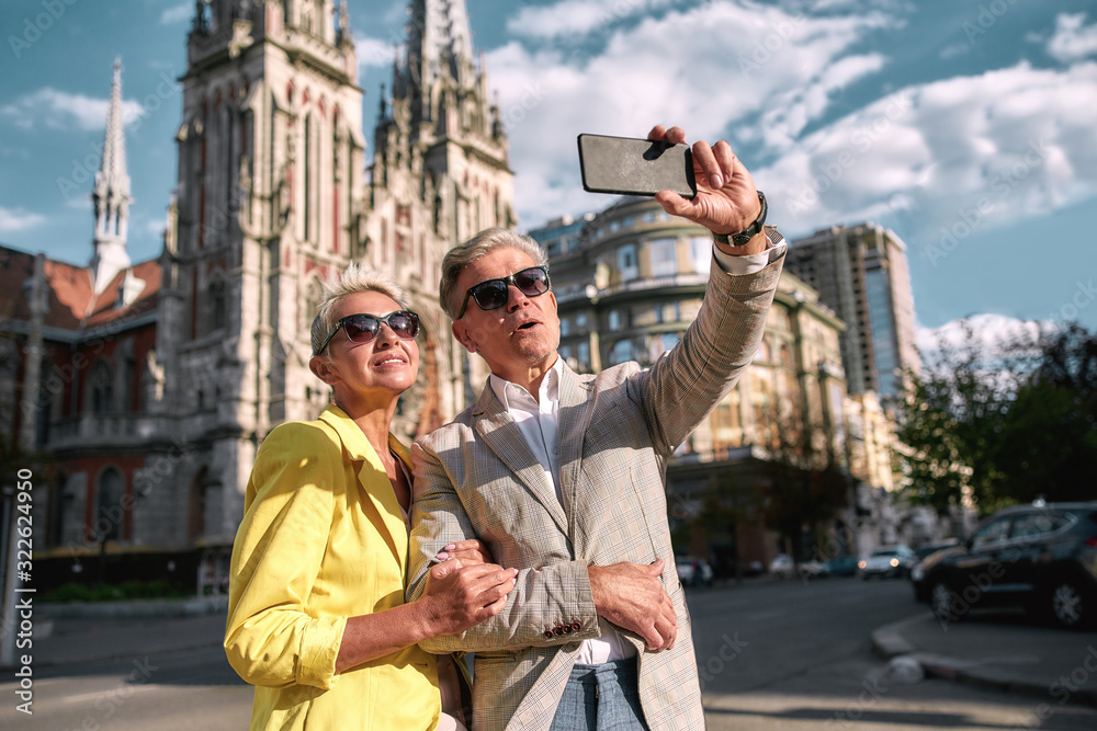 Fall in love. Happy and cheerful mature caucasian couple in sunglasses taking selfie by mobile phone and smiling while spending time together outdoors