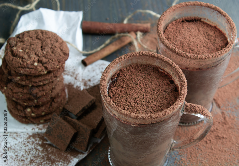 Two cups of hot chocolate on a wooden table with oatmeal cookies and chocolate
