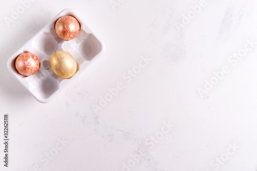 Ceramic egg tray with gold painted Easter eggs on white stone background, holiday concept