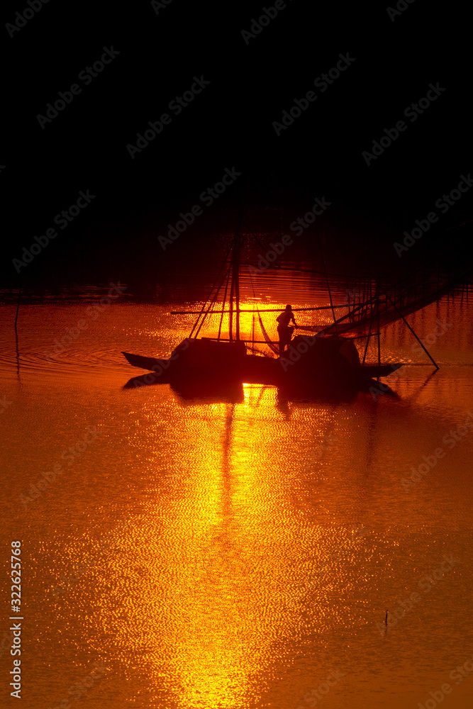 A traditional fisherman catching the fish Into the golden twilight at sunset time.