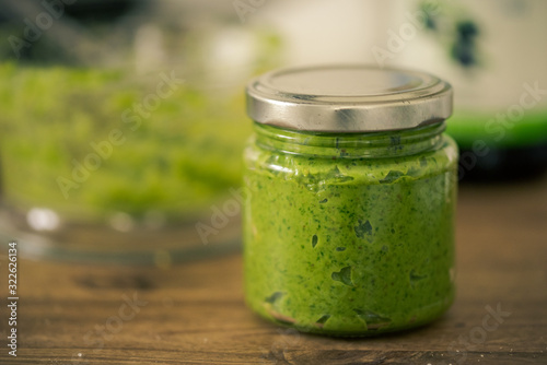 Obraz na płótnie Green pesto in reusable screw-top glass standing on dark wooden table with blurr