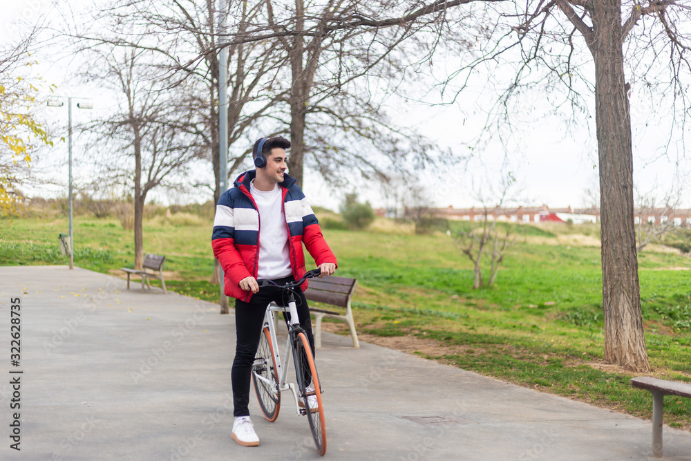Fototapeta premium Handsome hipster young man enjoying a bicycle ride and using a smartphone while listening music by headphones
