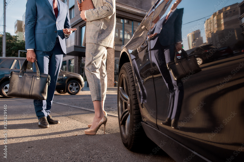 Obraz premium Cropped photo of two business people in classic wear standing near black car outdoors