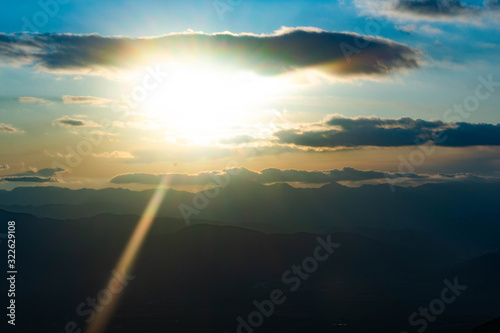 The sun between the clouds during a sunset and the mountains on the horizon