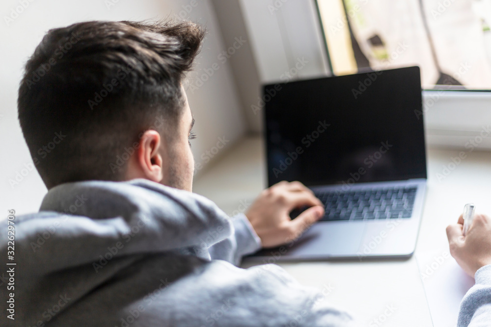 Rear view of a young man working with laptop on desktop at home Rear view of a young man working with laptop on desktop at home