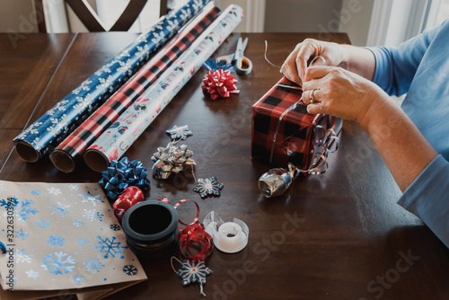 Hands wrapping present with gift wrapping supplies on table.