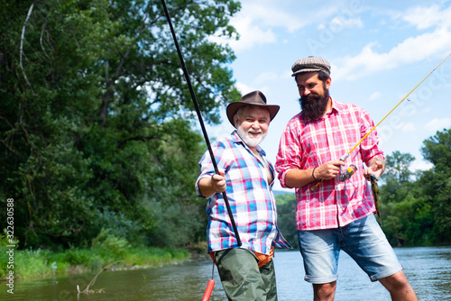 Fishing as holiday. Happy fishermen in water. Slightly older. Nice day for fishing. Men relaxing nature background. Summer leisure. Hobby and sport activity. Retired father and mature bearded son.