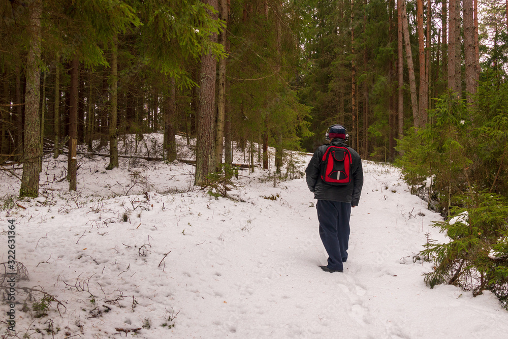 A man with a backpack of headphones walks along the winter forest path from us.