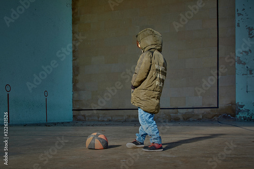 Boy with his hands in his pockets next to a deflated basketball ball. photo