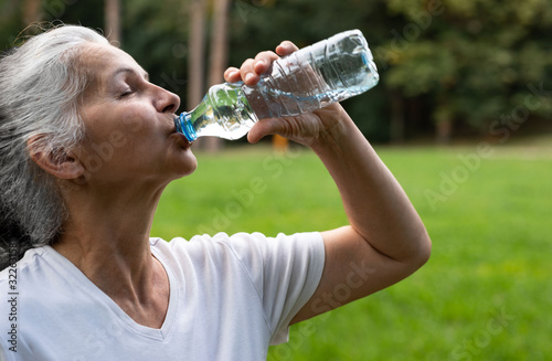 A beautiful senior woman is drinking water in the nature