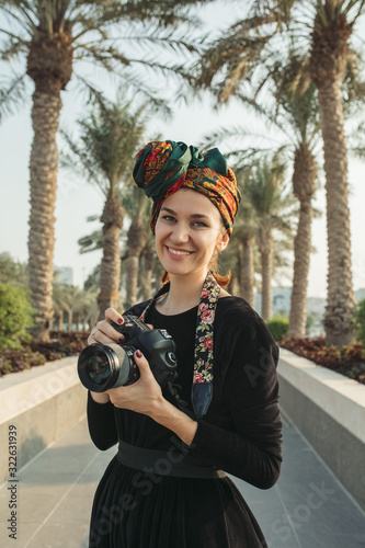 Portrait of smiling  young woman with headwrap holding her camera photo