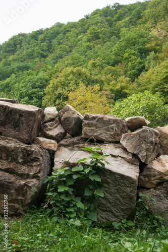 A fence of huge stone boulders laid on top of each other on a mountain slope against the backdrop of a mountain landscape.