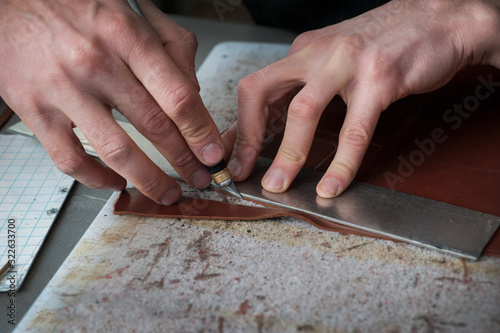 hands of master cutting with a knife pattern from genuine leather closeup