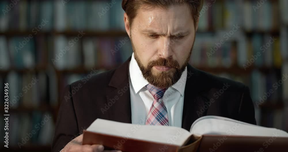 Handsome bearded male in business suit and tie reading book in library, new knowledge Handsome bearded male in business suit and tie reading book in library, new knowledge