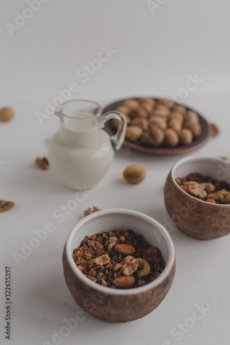 A healthy breakfast of granola, oatmeal, cereals, nuts and milk. Cups with granola, a jug of milk, a plate with nuts on a white background.