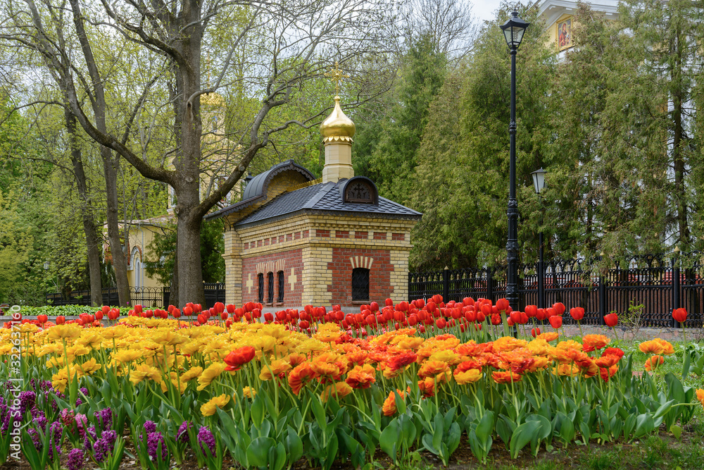 Chapel and tomb in Gomel park. Spring. Many tulips in the Gomel park. The facade of the chapel is made of carved stone and art metal, red unglazed terracotta and multicolor majolica, smalt mosaic. Chapel and tomb in Gomel park. Spring. Many tulips in the Gomel park. The facade of the chapel is made of carved stone and art metal, red unglazed terracotta and multicolor majolica, smalt mosaic.