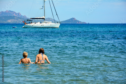 Two children stand in the sea, with yacht in the background © Claudia Evans 