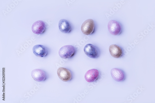 Colored painted pearl chicken and quail eggs of pink, silver, golden and blue color on a light blue pastel background. Minimalistic creative classic easter festive flat lay. Copyspace for text
