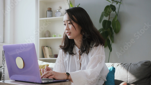 Gorgeous Caucasian girl sitting at table, using violet laptop, talking on video call. Footage of adorable young Chinese woman. Indoors. Technology. Apartment.