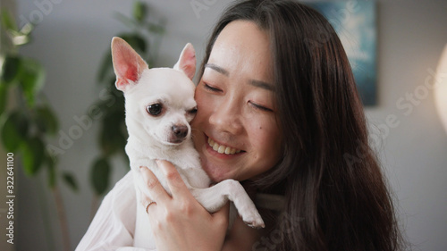 Beautiful young Chinese woman kissing lovely dog. Ancient breed. Dogtime. White Chihuahua and female owner spending time together. Indoors.