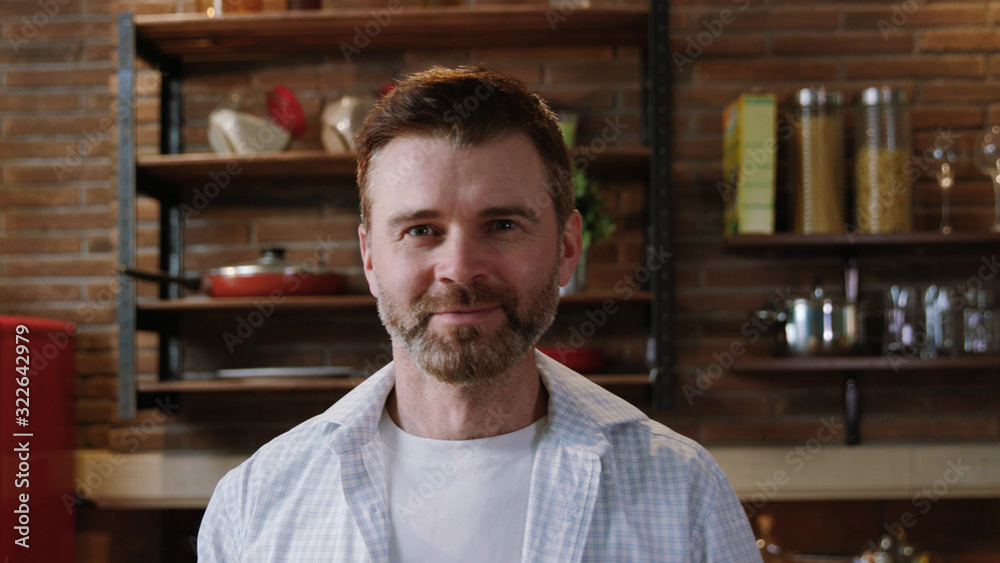 Lovely portrait of a happy smiling mature man in shirt with beard standing by a kitchen table staying at a luxurious home apeartment. Lovely portrait of a happy smiling mature man in shirt with beard standing by a kitchen table staying at a luxurious home apeartment.