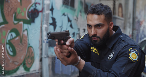 Police on duty. Portrait of severe bearded police officer holding aiming handgun looking forward. Crime scenein the city center.