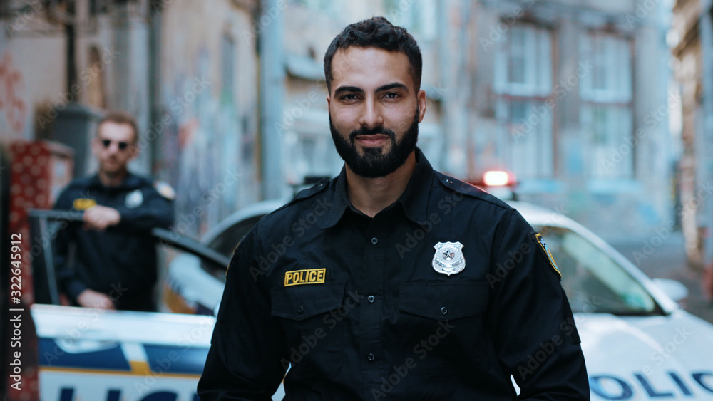 Strong smiling young man cops stand near patrol car look at camera enforcement officer police uniform auto safety security communication control policeman close up slow motion Strong smiling young man cops stand near patrol car look at camera enforcement officer police uniform auto safety security communication control policeman close up slow motion
