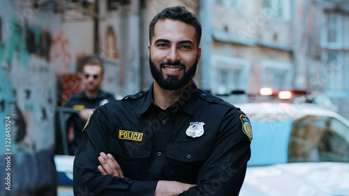 Fotografering Smiling young man cops stand near patrol car look at camera enforcement happy of