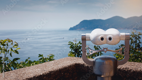 Touristic metal binoculars on sea shore. Coin operated binocular viewer on blurred background of sunset and sea. Shallow depth of field. Selective focus.