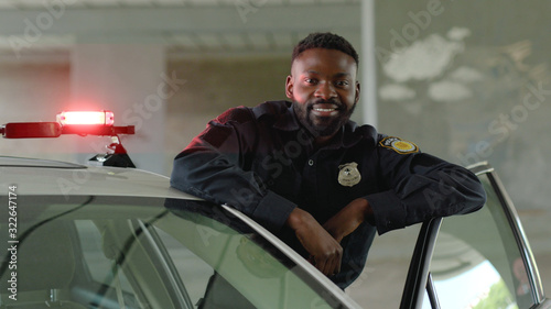 Smiling african american young man cops stand near patrol car look at camera enforcement happy officer police uniform auto safety security communication control policeman close up slow motion