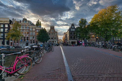 Photography Sunset cityscape from the streets of amsterdam with bikes, people riding bikes a