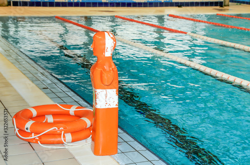 Maniquí de salvamento junto a dos flotadores salvavidas en el suelo junto a una piscina 