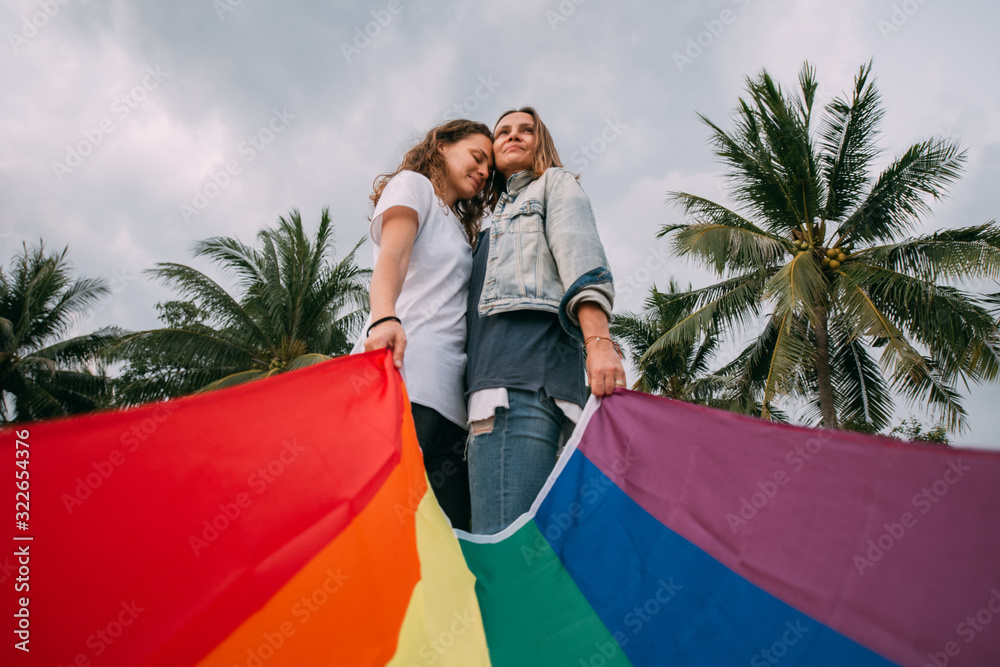 Two women with rainbow flag on the beach on a background of palm trees