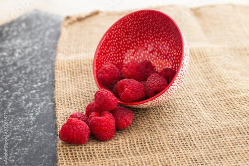 Red raspberries falling from a ceramic plate in a rattan and black background. Stylish superfood photography