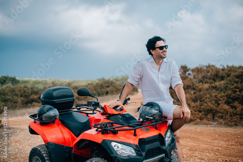 A man with a helmet in his hands next to the ATV