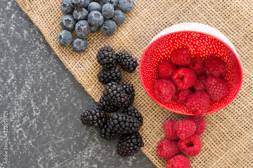Mix of Red raspberries falling from a ceramic plate and a bunch of blackberries and blueberries in a rattan and black background. Stylish superfood photography