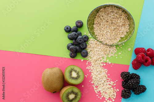 Rolled oat falling from a ceramic plate with a mix of kiwis, blackberries, raspberries and  blueberries in very colorfull background. Stylish superfood photography. Healthy breakfast