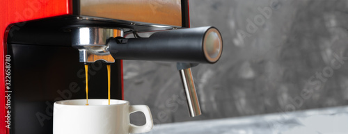 Red coffee maker pouring hot espresso coffee in a white cup. Coffee is poured through a portafilter into a coffee Cup.
