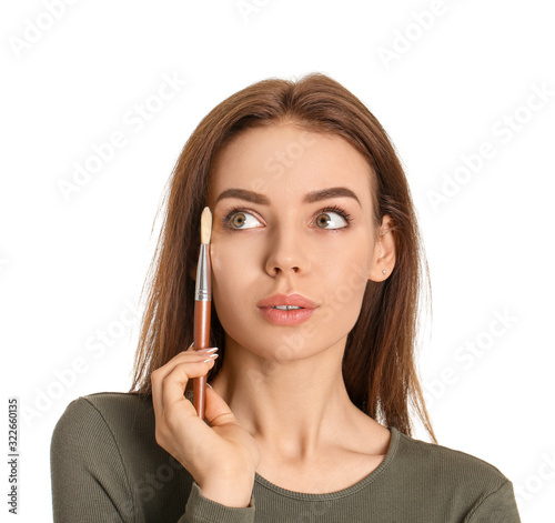 Beautiful young woman applying makeup on white background